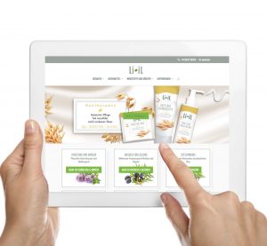 Der Website Relaunch der Li-iL Website wird gezeigt. Zwei Hände halten ein Tablet in der Hand und auf dem Tablet ist die neue Startseite der Li-iL Webseite abgebildet. Oben ist das Logo mit entsprechender Navigationsleiste abgebildet, darunter ein großes Banner, auf dem die "Hautzart"-Serie beworben wird und darunter werden verschiedene Themen, wie bspw. "Erkältung und Abwehr", "Muskeln und Gelenke" etc. angezeigt.