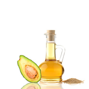 Eine Ölflasche mit einem Korken, die bis zum Rand mit Öl gefüllt ist. Neben der Flasche liegen kleine Saaten und eine aufgeschnittene Avocado.