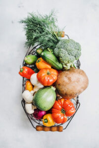 Ein gut gefüllter Korb mit einigen Gemüsesorten und verschiedenen Kräutern. Im Korb liegen unter Anderem ein großer Brokkoli, Pilze, Zucchini, Paprika, Pilze und Dill.